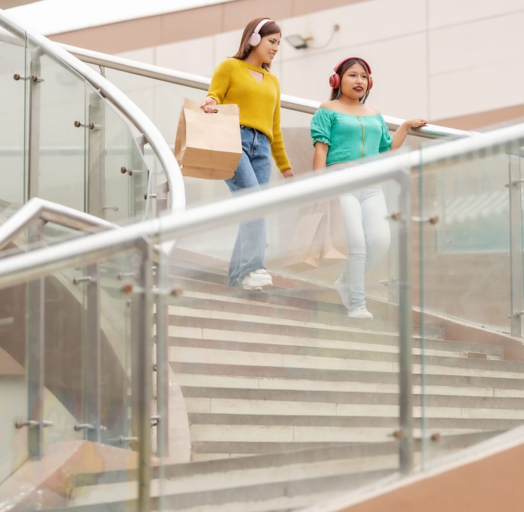 Two latin friends walking down a stairs with shopping bags in a mall